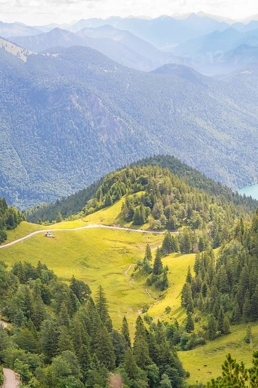 View over green hills and forests with mountain ranges in the background, Herzogstand summit, Walchensee, Schlehdorf, Germany