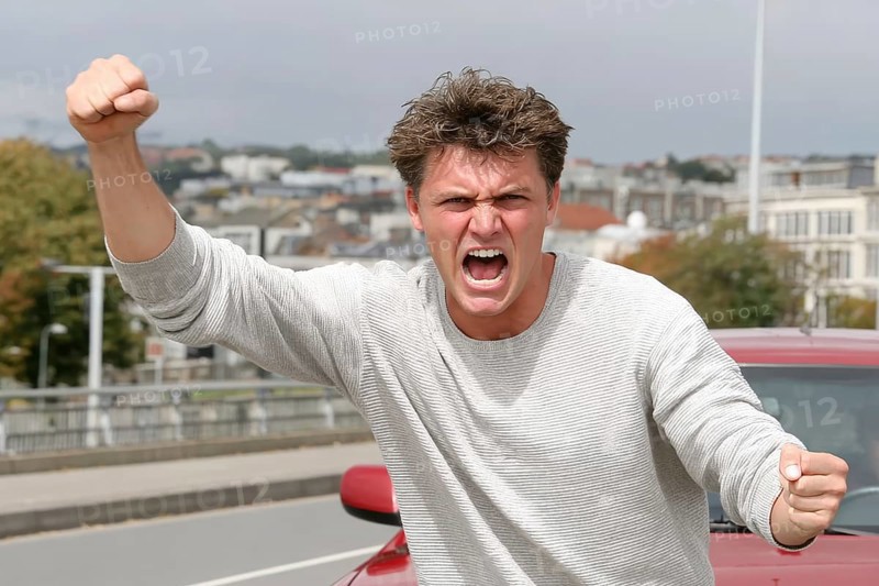 A man shouts angrily with clenched fists on a road, symbolic image for aggressive behaviour in road traffic, AI generated