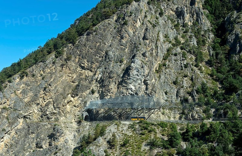 Yellow Swiss Post bus travelling under the safety nets against falling rocks to the Petits Pontis tunnel, cantonal road in Val d'Anniviers, Valais, Switzerland