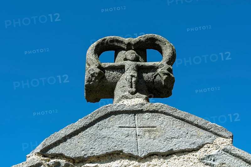Stone cross on the bridge over the Pavin couze river flowing through the village of Saurier, Puy de Dome. Auvergne Rhone Alpes, France