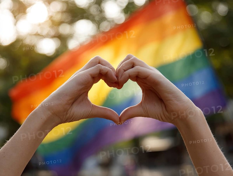 Two hands form a heart in front of a waving rainbow flag in the sunlight, symbolising equality, tolerance and diversity, AI generated, AI generated