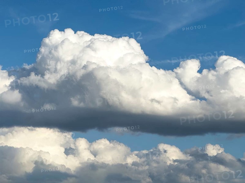 Stratocumulus in the centre of the picture, dense cloud cover from many cumulus clouds in the background, bright blue sky above, international