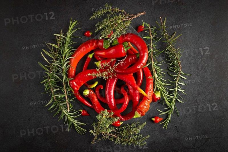 Red peppers, chilli peppers and herbs arranged on a dark background
