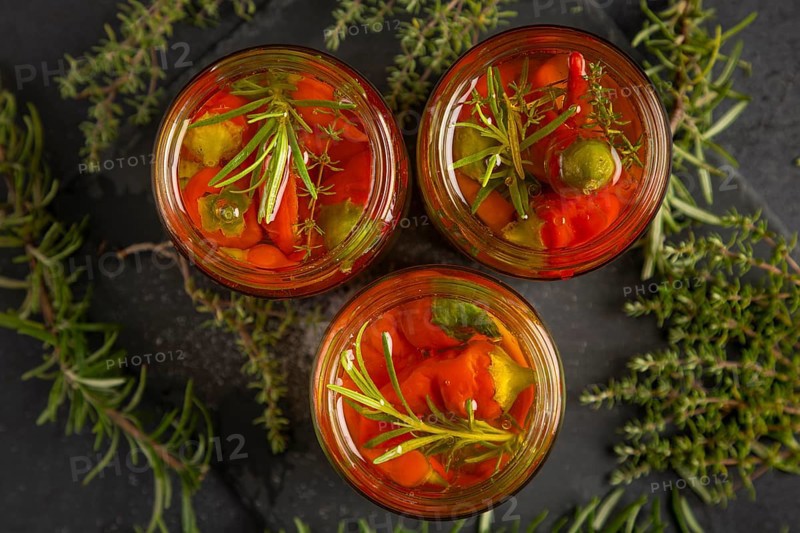 Top view of three jars of herbs and chilli peppers surrounded by rosemary and thyme