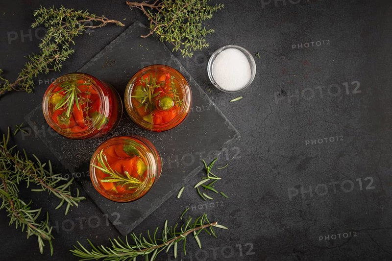 Three glasses filled with pepperoni and herbs on a dark surface next to salt