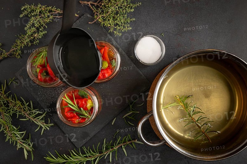 Cooking pot with vinegar, jars with chilli peppers and herbs on a dark background