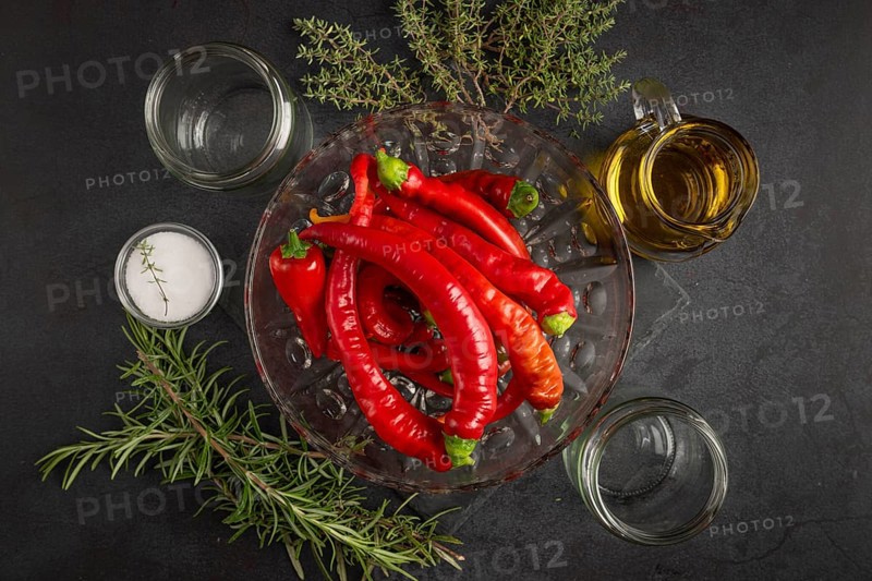 Several red peppers, chilli peppers alongside oil, salt, herbs and empty jars