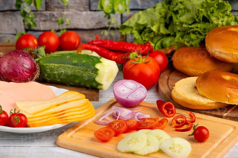 Bagels alongside sausage, cheese and fresh vegetables such as tomatoes, lettuce, cucumber and peppers