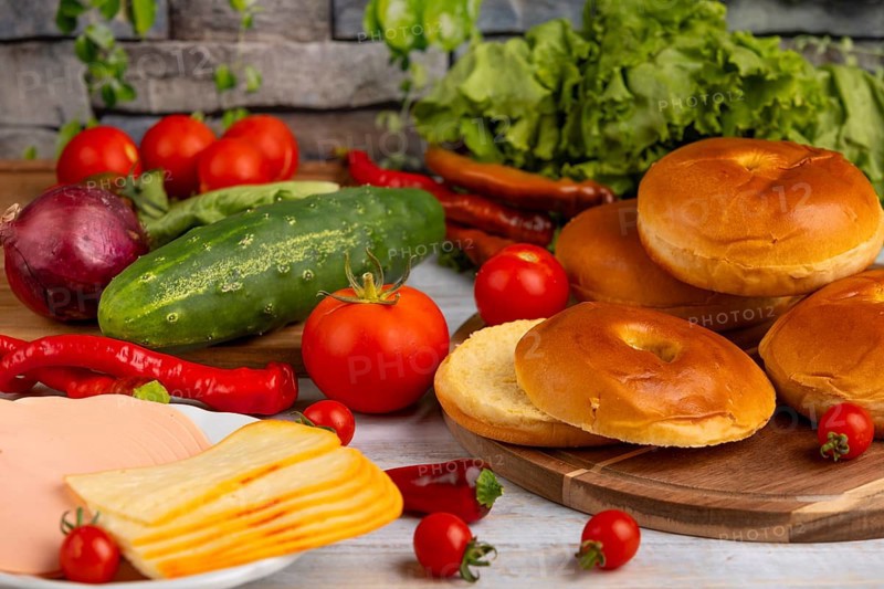 Bagels alongside sausage, cheese, fresh vegetables such as tomatoes, lettuce, cucumber and peppers