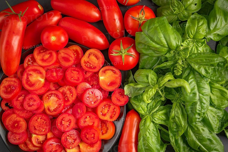 Fresh sliced tomatoes and basil on a dark-coloured surface