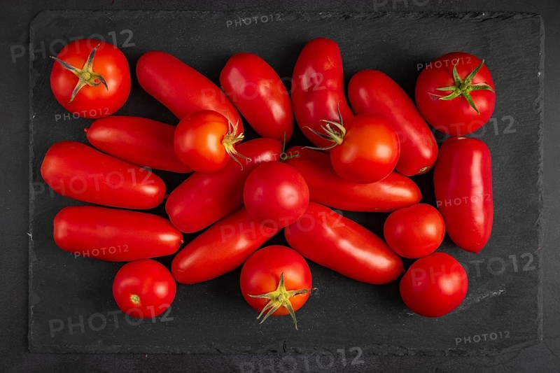 Different types of tomatoes lie on a dark slate slab