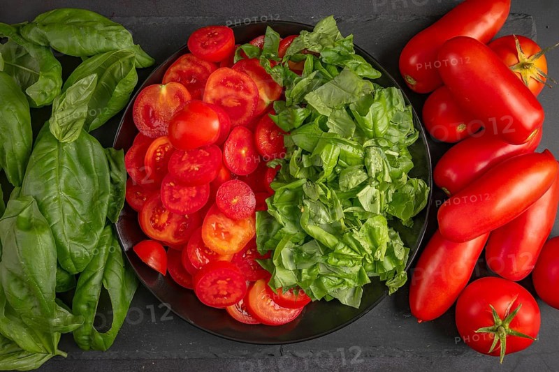 Sliced tomatoes and basil on a black plate