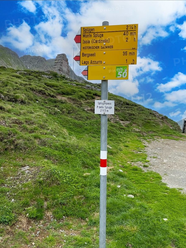 Information board Sign with arrow-shaped signpost at the top of the Splügenpass Passo dello Spluga Signpost for mountain hikers with the inscription Splügen Monte Spluga Bergseeli Lago Azzurro, Splügenpass Passo dello Spluga, Lombardy, Italy, Grisons, Switzerland
