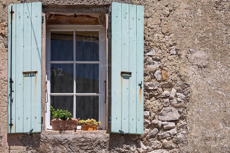 A window with blue shutters in a rustic house wall with flowering potted plants, Provence, France