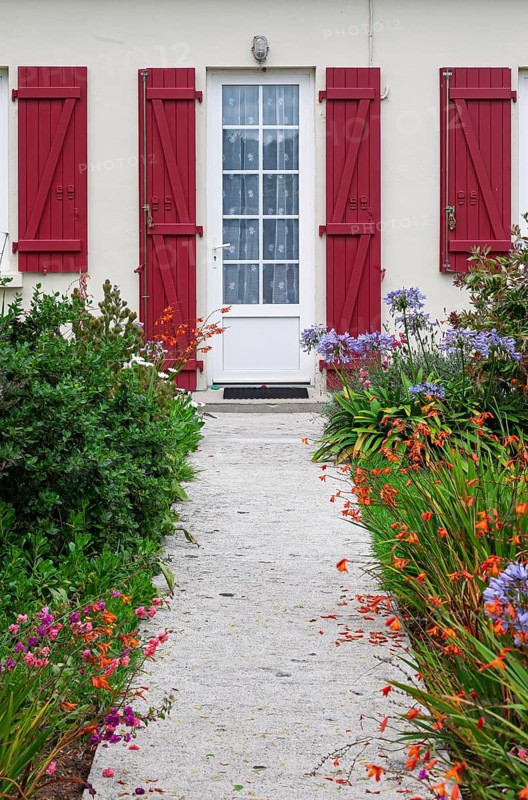 House façade with mullioned windows, entrance door and red shutters and flower beds, Ile de Brehat, Brittany, France
