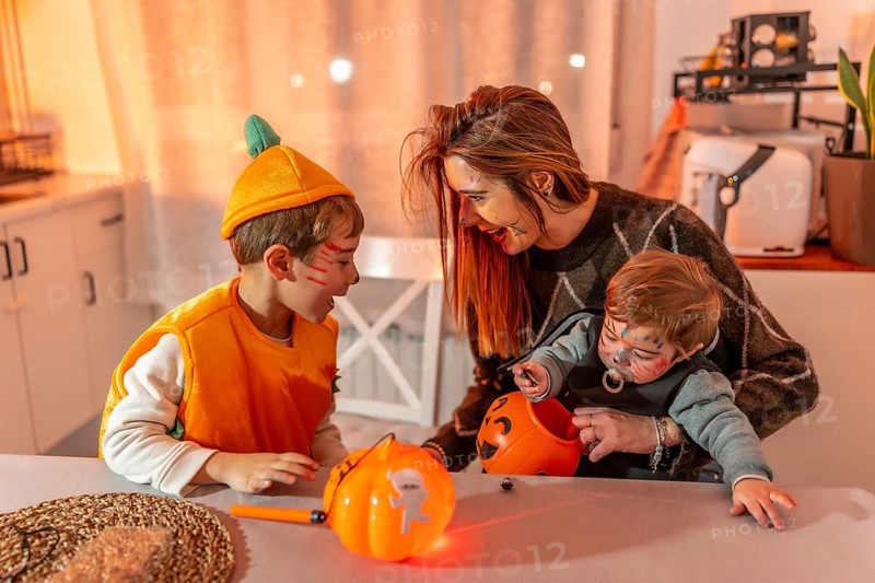 Mother and children wearing halloween costumes are sitting at a table in their kitchen, playing with pumpkin baskets full of candies