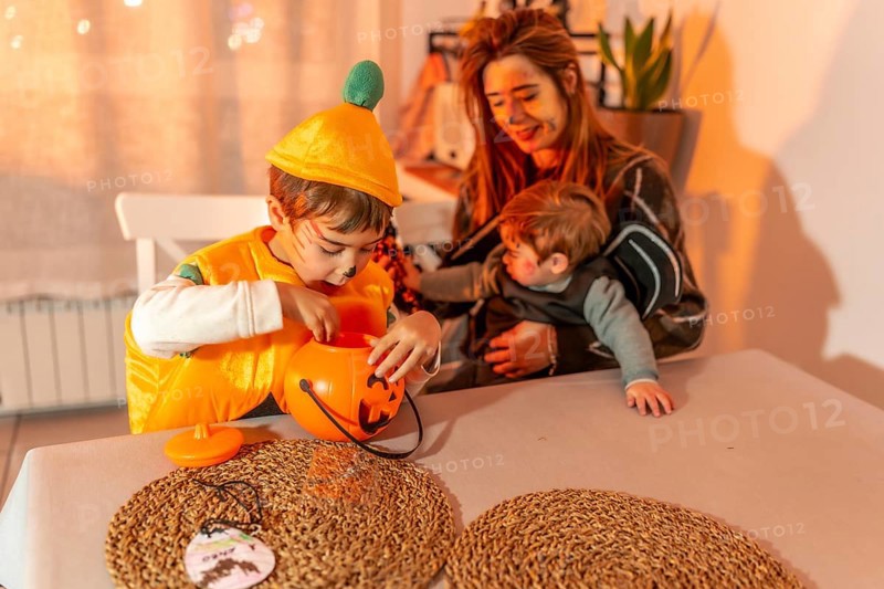 Two young brothers wearing halloween costumes are playing at a table with their mother, enjoying the festive atmosphere