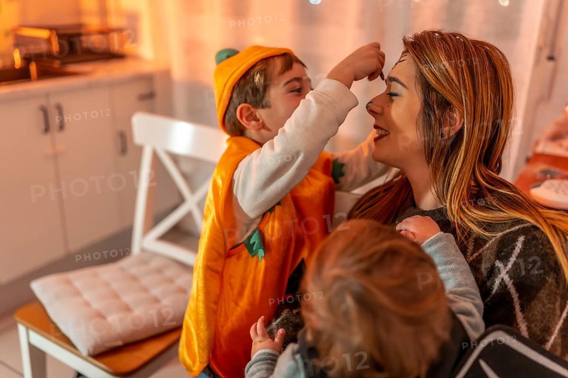 Happy family preparing for a halloween party, applying colorful makeup together at home, creating joyful memories in a cozy atmosphere