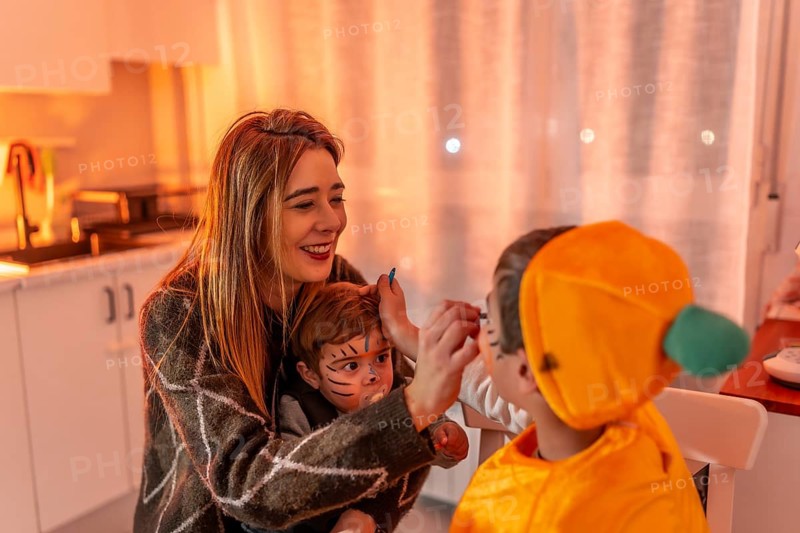 Happy family preparing for halloween party, mother applying makeup on children's faces, creating festive atmosphere