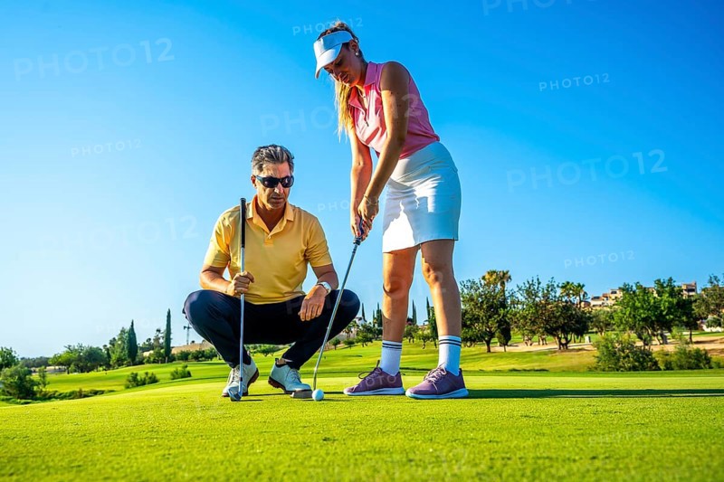 Golf instructor guides a woman on the putting green, focusing on technique under a clear blue sky. Perfect day for learning and practicing golf