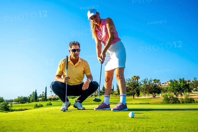 Female golfer receiving putting advice from her instructor under the warm sun, focusing on technique and skill improvement at the golf course