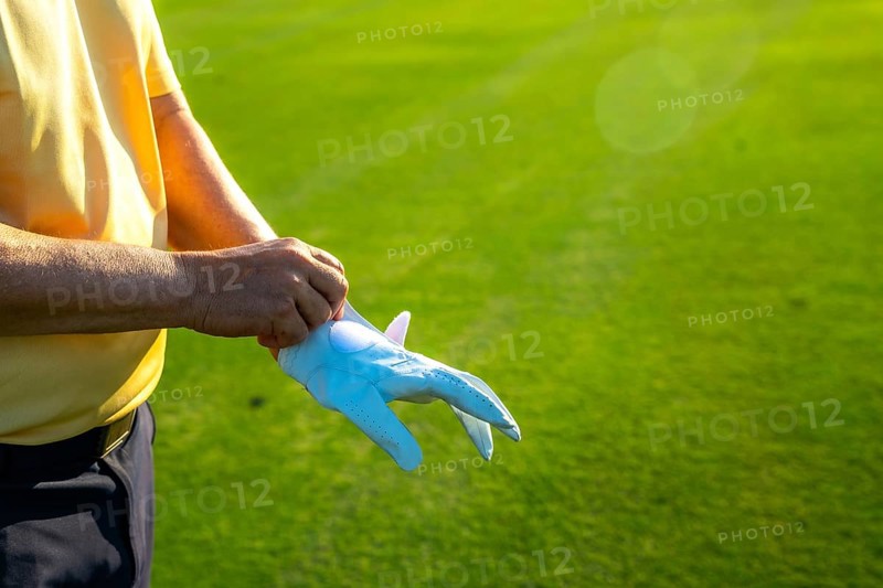 Golfer putting on a white glove, getting ready for an exciting game on a lush, vibrant green golf course under the sunny sky