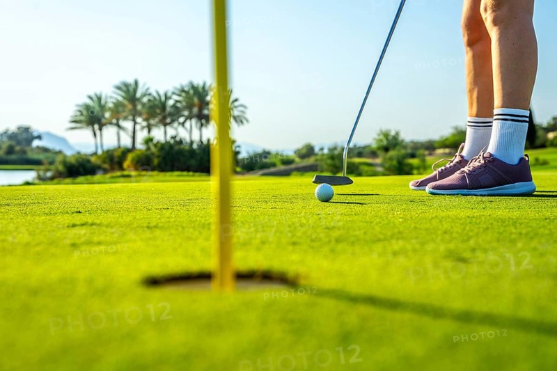 Golfer putting ball on green towards hole on sunny day, low angle view focusing on the action and the precision of the sport