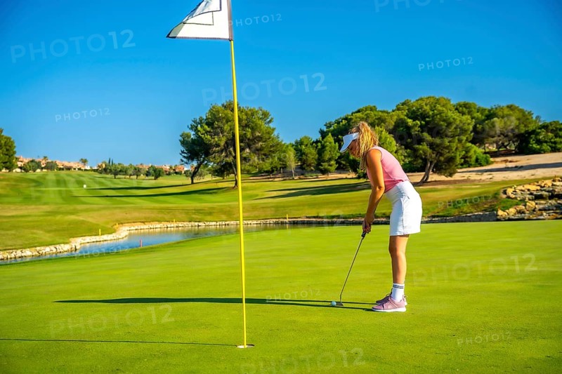 Female golfer concentrating on putting the ball on a sunlit day, enjoying the beauty of a lush golf course surrounded by nature