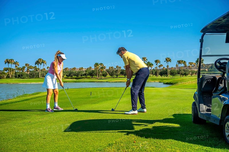 Father and daughter duo playing golf on a sunny day, surrounded by palm trees and a clear blue sky, enjoying quality time on the course