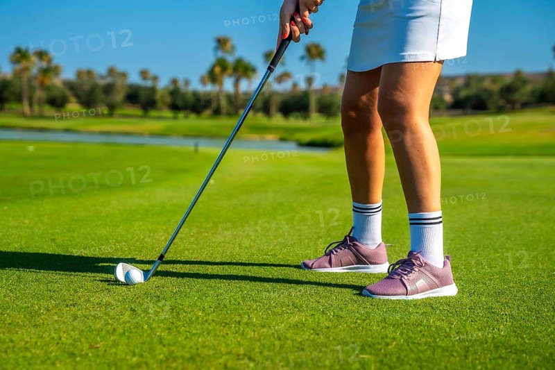 Female golfer concentrating intensely while hitting the golf ball on a bright, sunny day at the lush green golf course