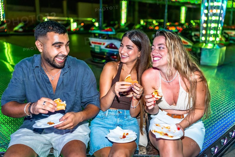 Happy friends enjoying burgers and pizza at amusement park, having fun together on a summer night out