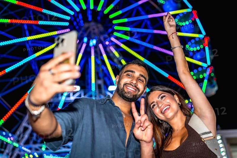 Joyful friends capturing a selfie with a vibrant ferris wheel in the background, celebrating a fun night at the carnival