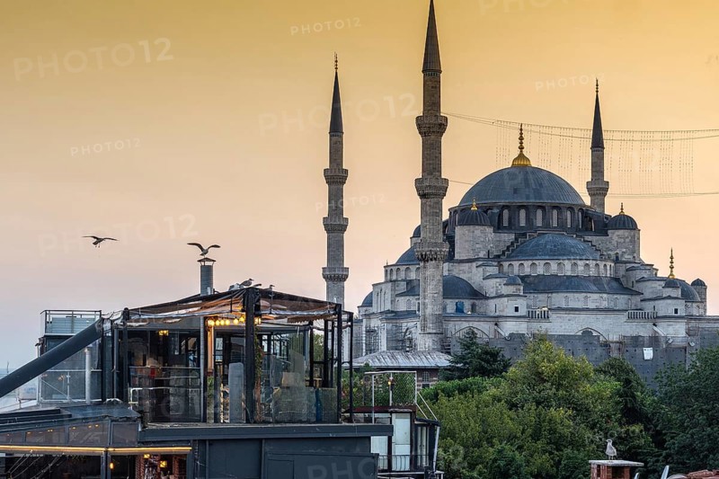 Seagulls flying over a rooftop restaurant in istanbul, turkey, with the sultan ahmed mosque in the background at sunset