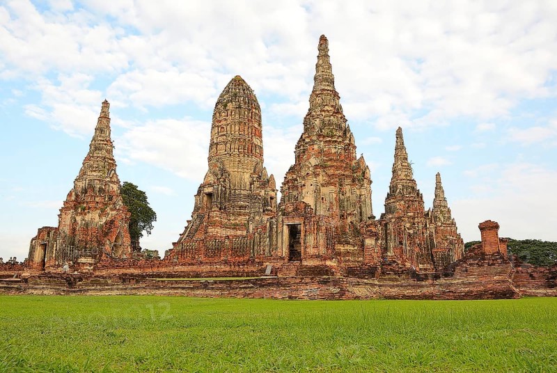 Scenic view of the historical wat chaiwatthanaram temple with its towering prangs and serene green lawn under a cloudy sky in ayutthaya, thailand