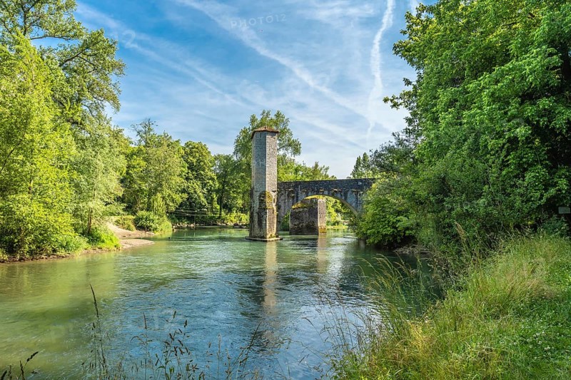 Scenic view of the historic stone bridge over the gave d'oloron river, surrounded by lush greenery, in the charming town of sauveterre de bearn, france