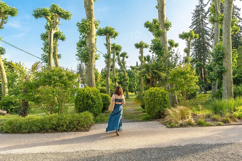Young woman enjoying a sunny day walking in a park with pruned plane trees and lush vegetation in salies de bearn, france, during summer vacation
