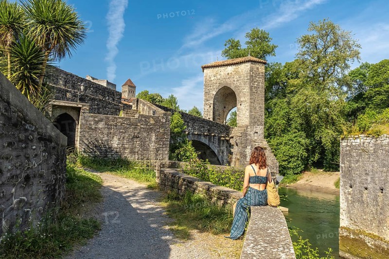Young woman enjoying the scenic view of the historic bridge and fortifications in sauveterre de bearn, a charming medieval town in the pyrenees atlantiques region of france
