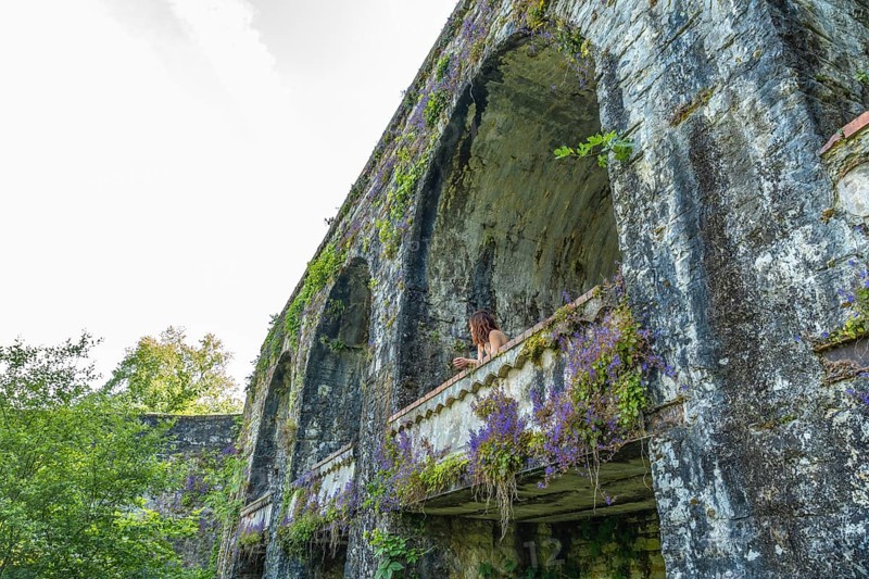 Tourist admiring the landscape from a balcony of an ancient aqueduct covered in vegetation in sauveterre de bearn, france
