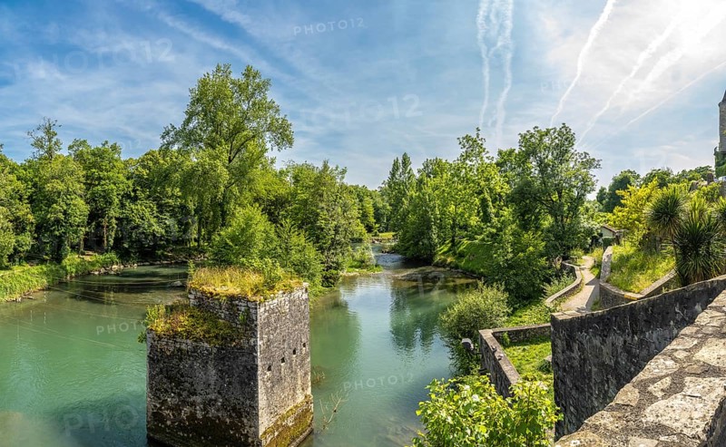 Scenic view of the gave d'oloron river with a ruined bridge pier and lush vegetation in sauveterre de bearn, a charming medieval town in the pyrenees atlantiques region of france