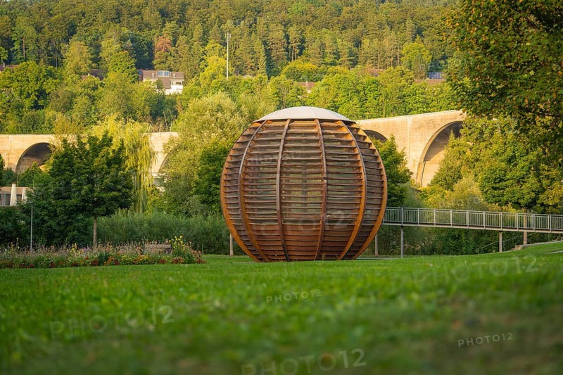 Large wooden ball in front of a bridge, surrounded by green trees and grassland, Nagold, district of Calw, Black Forest, Germany