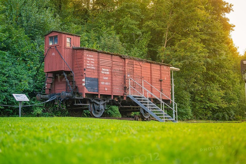 A red goods wagon with steps, green meadow and forest next to it. Nostalgic railway environment, Nagold, district of Calw, Black Forest, Germany