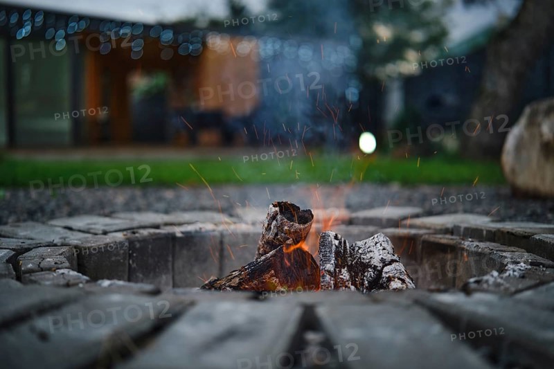A fire pit crackles with bright flames and glowing embers, surrounded by rustic stones