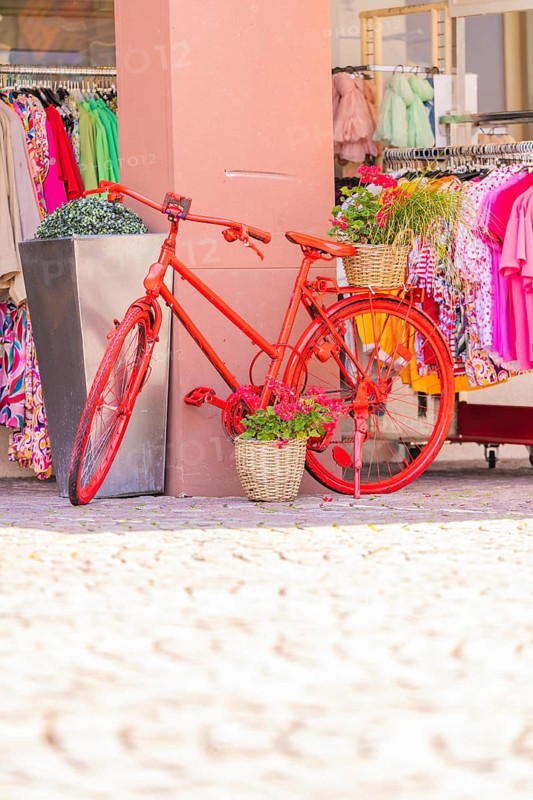 Red bicycle decoratively in front of a clothing shop, surrounded by colourful clothes, small town of Perle Calw, Black Forest, Germany