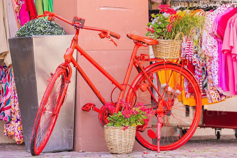 A decorated red bicycle stands in front of a clothing shop with colourful clothes, small town of Perle Calw, Black Forest, Germany