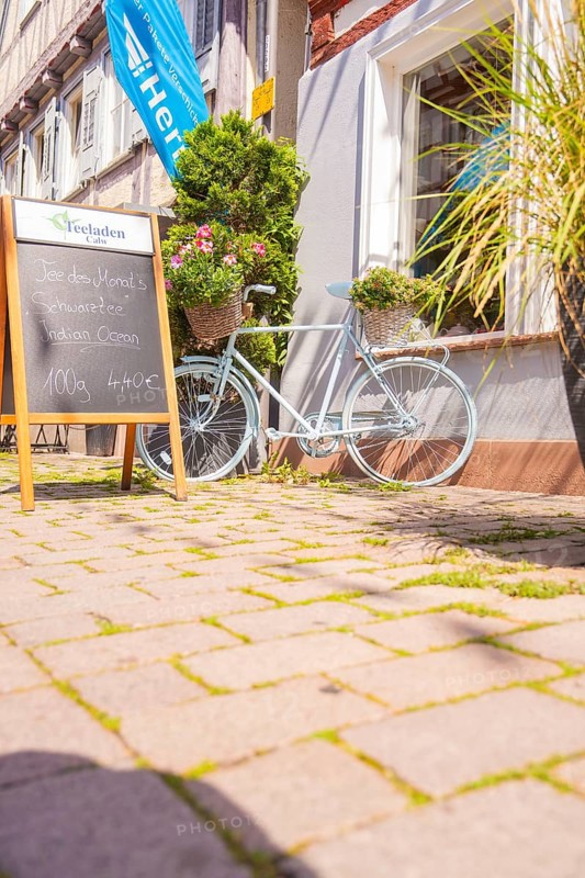 Bicycle with flower baskets and chalkboard in front of a café in the sunshine, small town of Perle Calw, district of Calw, Germany