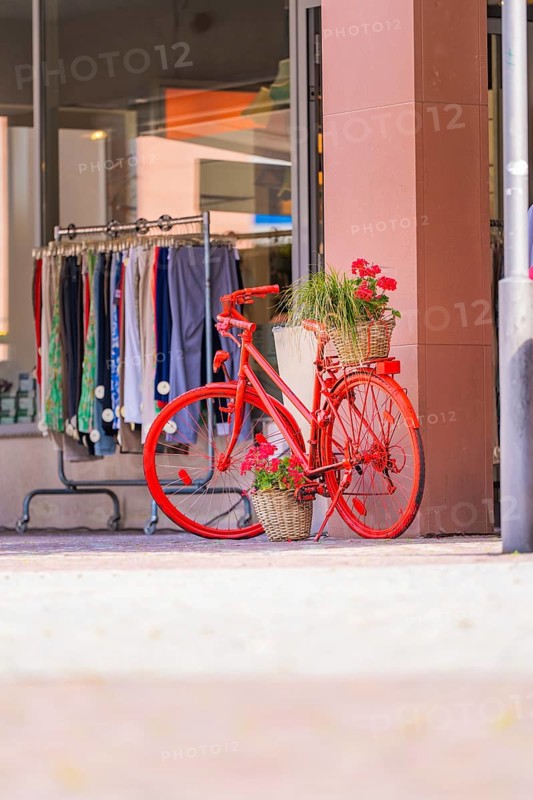 Bright red bicycle with flower arrangement in front of a fashion shop in a sunny street, small town Perle Calw, Black Forest, Germany