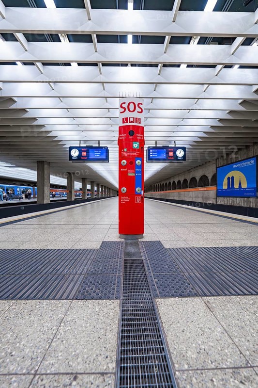 A central SOS pillar in a modern railway station concourse with empty platforms, Munich, Germany