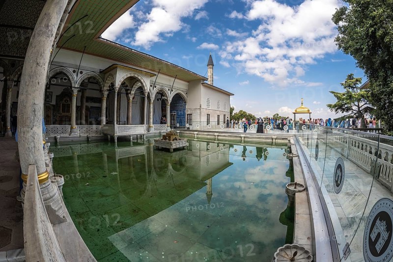 Tourists walking around the courtyard with reflecting pool of the topkapi palace in istanbul, turkey, on a sunny day