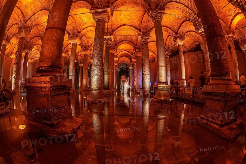 Tourists walking on a walkway in the basilica cistern in istanbul, turkey, with warm light reflecting on columns and water