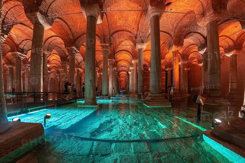 Tourists walking on a walkway in the basilica cistern, a historical landmark in istanbul, turkey, with turquoise illuminated water and ancient columns